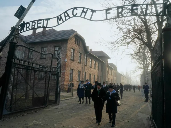 Holocaust survivors walk through the infamous entryway of Auschwitz.